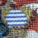 Figure 7 - King George III Golden Jubilee Quilt, 1810, England. Museum no. T.25-1961. Detail of a purple and white striped cotton fabric from the previous quilt top seen through a hole in the present border fabric.