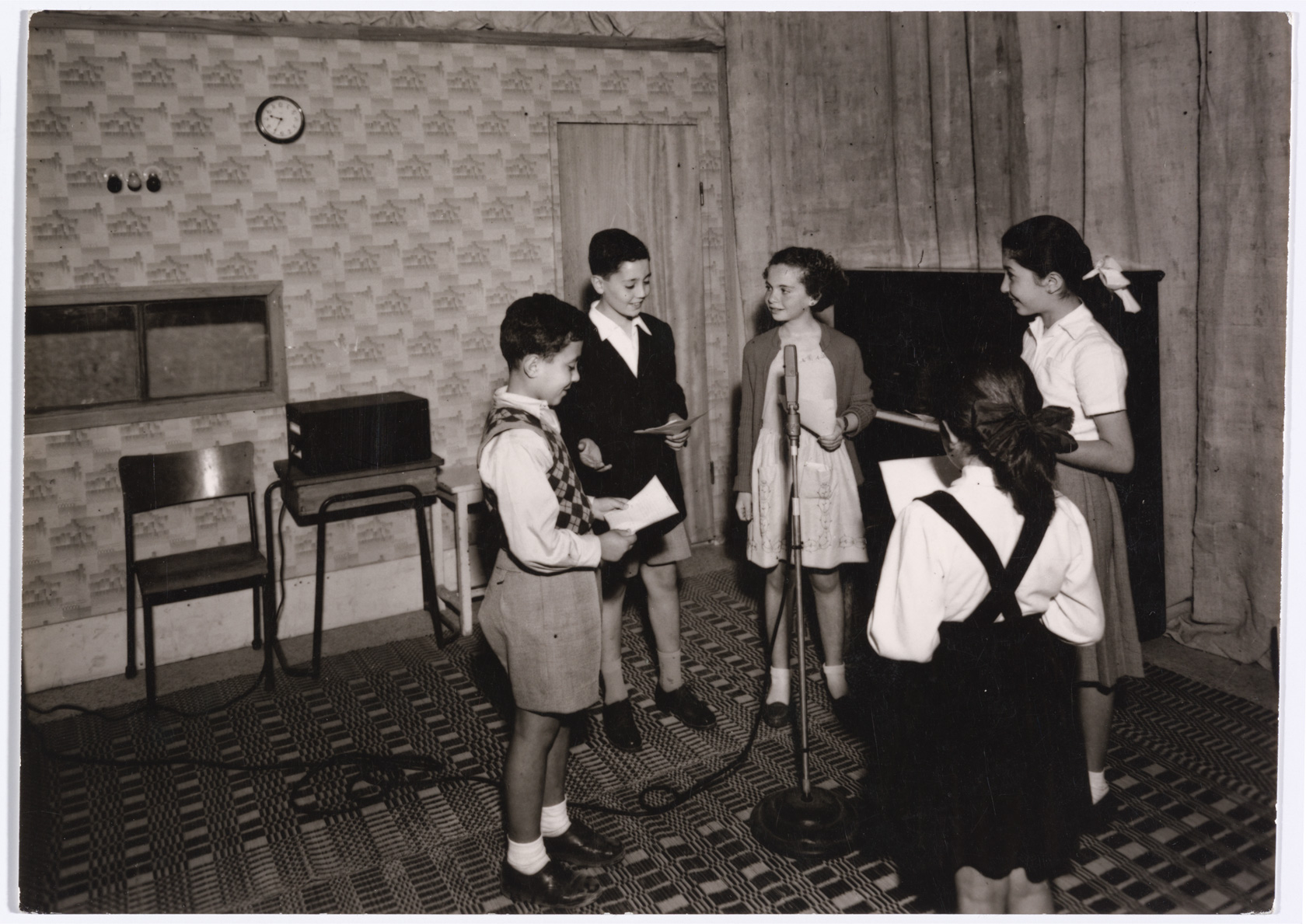 5 children surrounding a microphone smiling