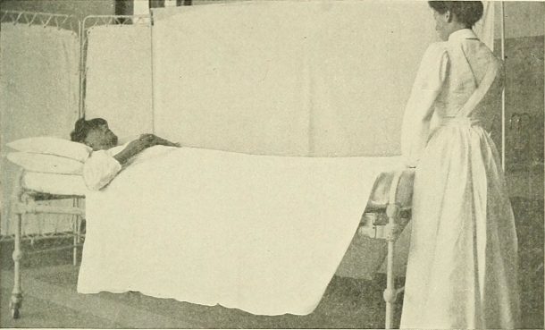 A woman lying in a bed, with a nurse standing by