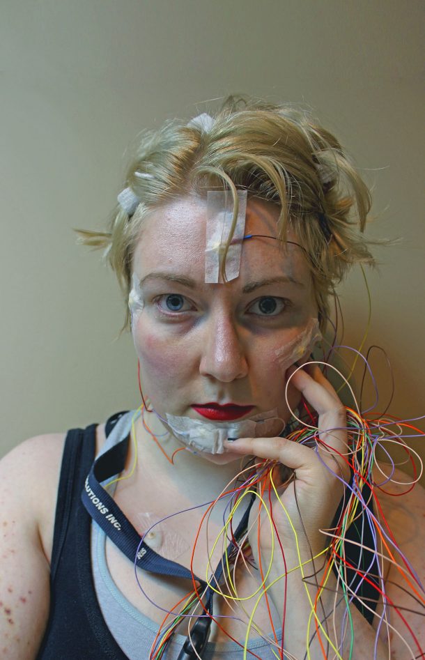 A non-binary person holding wires and looking at the camera