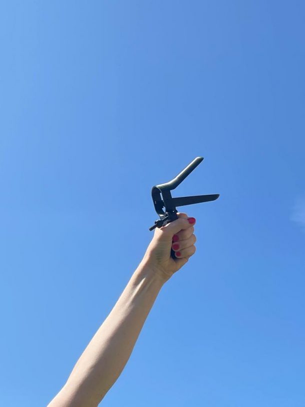 A hand holding a black speculum against a blue-sky background