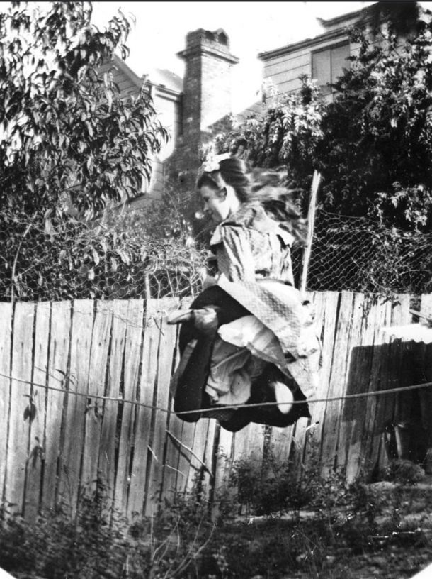 A girl skipping in a garden against a wooden fence