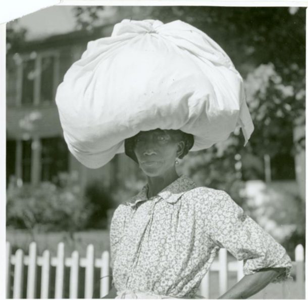 A woman carrying a large bundle wrapped in a sheet on her head.