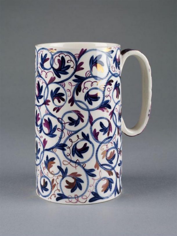 A decorated mug set against a grey background. The floral details are hand-painted.