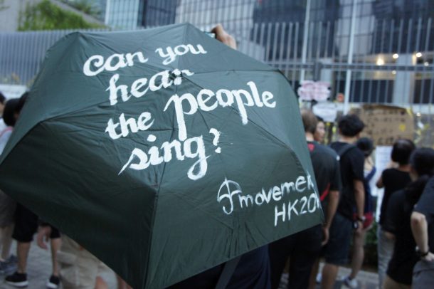 One of the umbrellas with calligraphy by Savona Ling, outside the first “Democracy Wall” on the tall fences encircling the Civic Square in the background. Civic Square, whose name was so given in a student movement against nationalist education in 2012, was fenced off in recent months for added security to the Central Government Offices. © Becky Sun