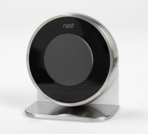Learning Thermostat by Nest Lab round thermostat with silver casing with a black screen. The thermostat slots on to a stand with a circular base.
