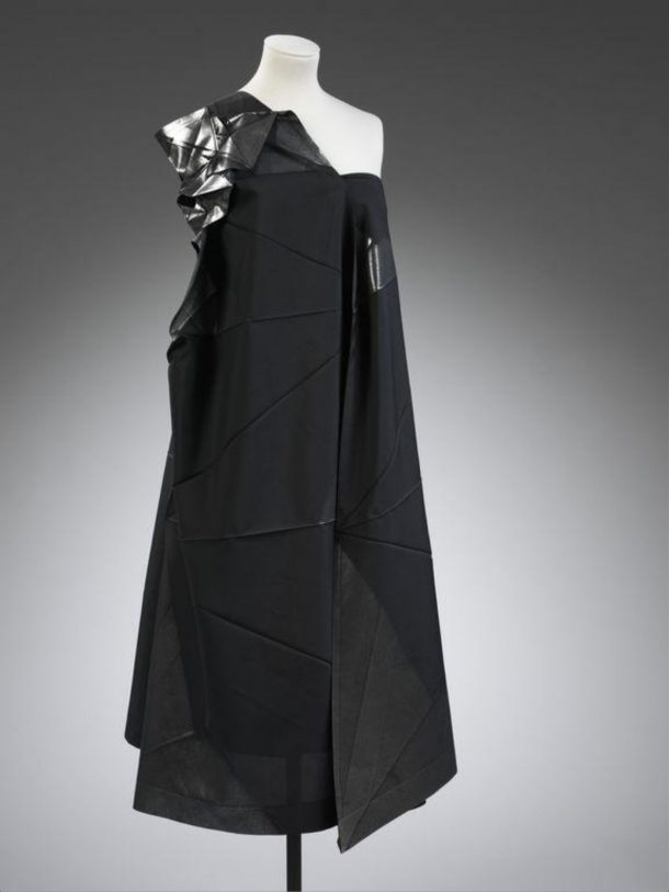 A black, angular dress – with careful fold marks and decorated shoulder piece