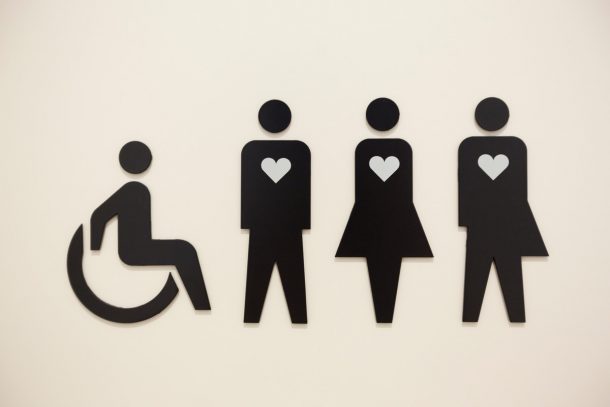 a sign on a toilet door showing four people in a line, one in a wheelchair and the other three with heart symbols on their chests.