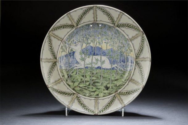 A round plaque decorated with a white deer running through a forest