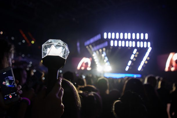 Someone holding up a light stick in a crowd in front of a stage.
