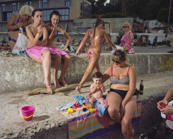 A group at the beach, wearing swimwear. Some of them are eating.