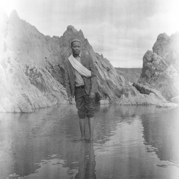 A youth standing in water against a mountainous background