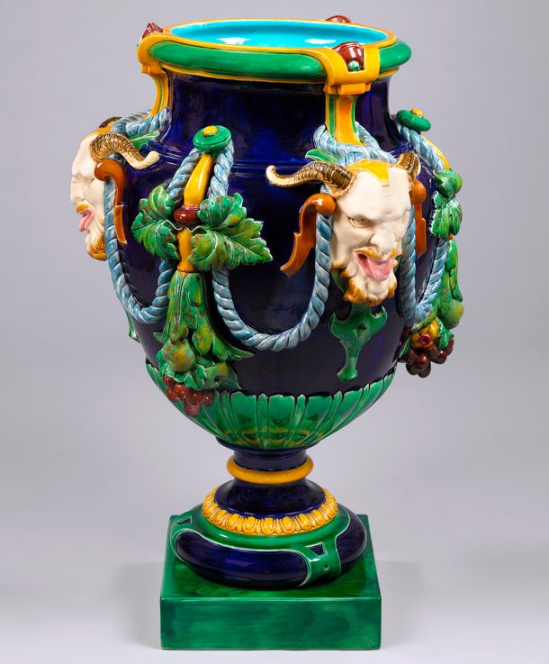 Blue, green and yellow majolica vase, featuring three satyr (half-man, half-goat) heads with their tongues out