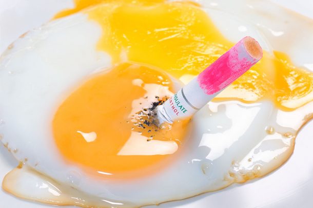 A cigarette end, covered in lipstick, stubbed out in a fried egg
