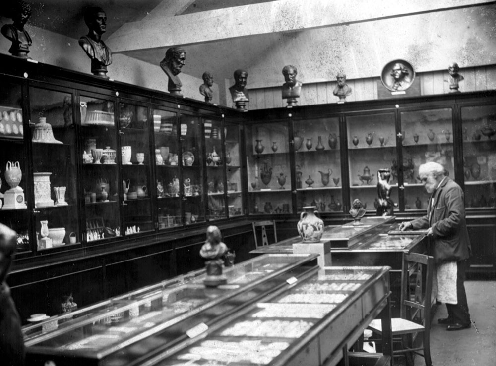 A bearded man looks at specimens in an old museum, with shelves behind him