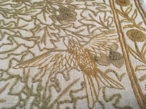 Close up of bird, leaves, acorn, and floral border in various brown wools