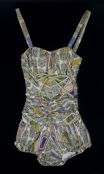 One-piece bathing costume in cotton, with a floral print in variegated colours, mainly yellow, green and blue. Pale green cord tie at the front. Elastic-ruched back. Wide shoulder straps, adjustable with buttons/buttonholes on the straps and back.