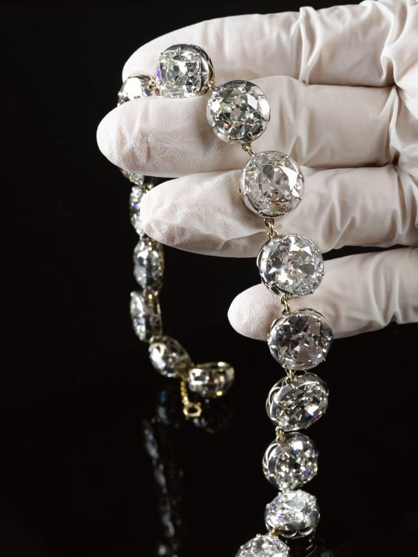 A white-gloved hand holding sparkling diamonds