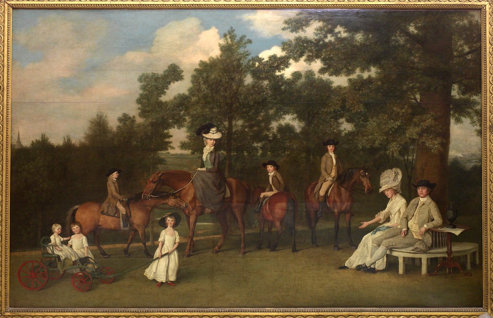 Family portrait group, with two people seated, four on horses and three children playing with a cart