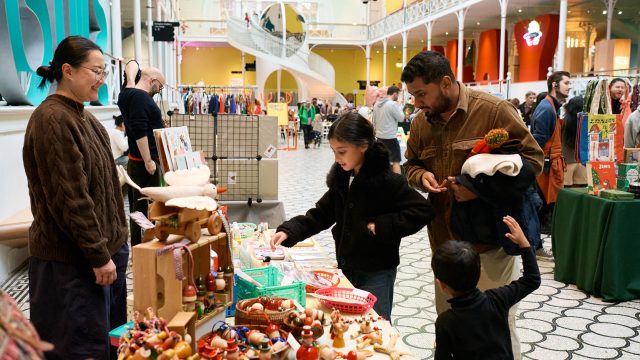 A family of 1 man and 2 children look at objects on a stall at a festive market