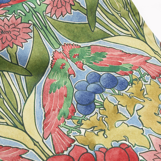 Detail of a cotton tea towel featuring a green and red botanical pattern with parrots.