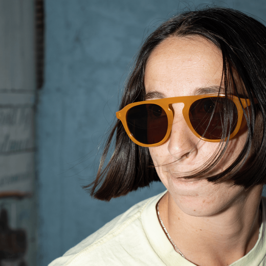 A woman with black straight hair modelling a pair of mustard coloured sunglasses.