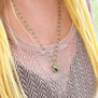 A blonde woman wearing a rosary gold necklace with green pendant.