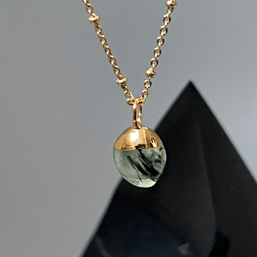 A pale green stone pendant on a gold chain necklace.