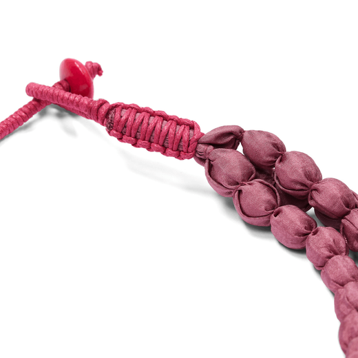 A detail of the clasp of a pink necklace made strands of textile beads.
