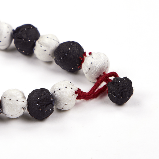 Close up of a bracelet composed of black and white fabric beads and red fabric clasp.