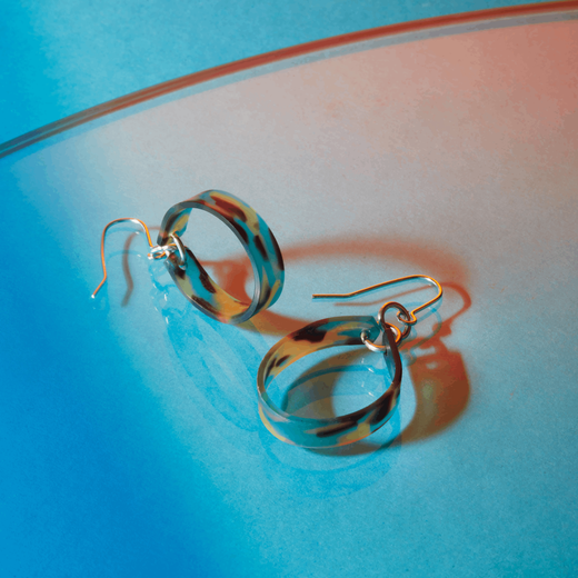 A pair of earrings featuring acetate hoops in shades of blue and brown and silver hooks.