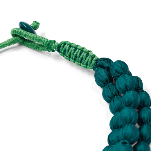 A detail of the clasp of a blue necklace made strands of textile beads.