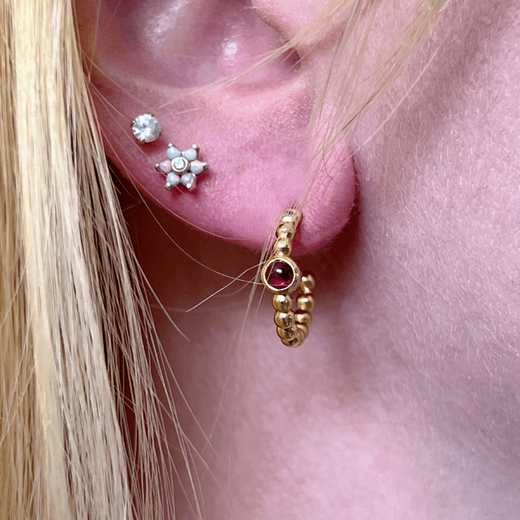 Detail shot of the ear of a blonde woman wearing three small earrings.