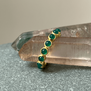 A gold ring with green onyx round stones photographed on a pink crystal. 