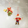 Two animal felt decorations hang from a tree branch in a snowy setting.