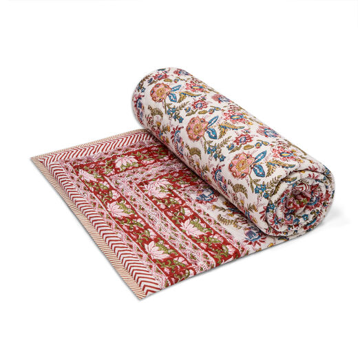 A rolled red and white quilt featuring a floral pattern.