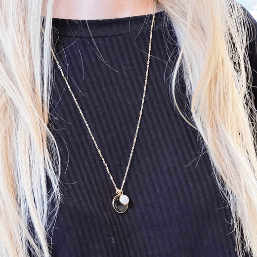 Close up of the neck of a blonde woman wearing a black top and a chain necklace.