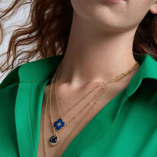 A model wearing two blue pendant necklaces on gold chains, on a bright green shirt.