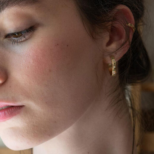 A young woman with dark hair wears a small hoop earring.