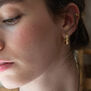 A young woman with dark hair wears a small hoop earring.