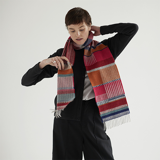 A white woman with dark short hair modelling a multicoloured winter scarf.