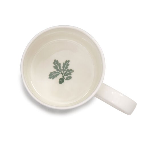 The inside of a white china mug with a green brach with oak leaves and acorns.