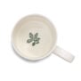 The inside of a white china mug with a green brach with oak leaves and acorns.