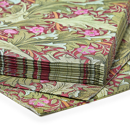 A stack of paper napkins featuring a green and red botanical Arts & Crafts pattern by John Henry Dearle.