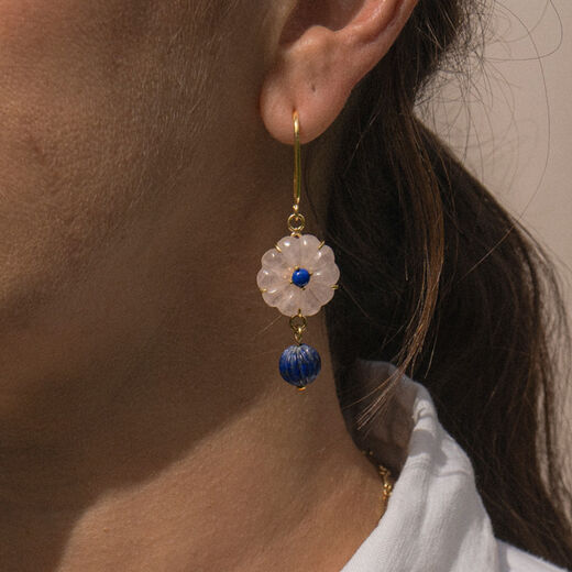 A close up of the neck and ear of a woman wearing a pink and blue flower shaped hook earring.