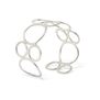A silver cuff bracelet made up of hoops of various sizes, propped standing on a white top.