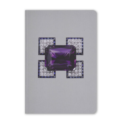 A grey pocket-sized notebook featuring an angular diamond brooch with a large purple amethyst at its centre