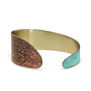 A brass cuff bracelet with a turquoise and brown coloured patina.