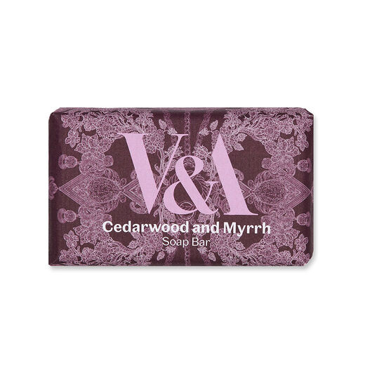 A soap bar wrapped in a purple and pink paper wrapping featuring an intricate illustration of jewellery and the V&A logo.
