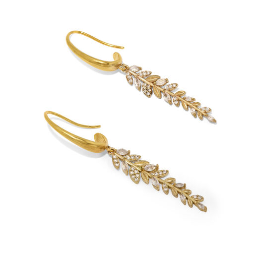 A detail of a pair of hook gold earrings. Each features a pendant in the shape of a long leaf branch with crystals.